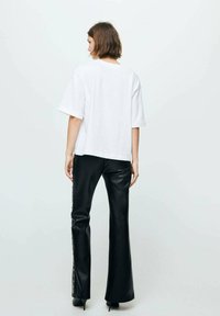T-shirt blanc surdimensionné à manches courtes, associé à un pantalon évasé en simili cuir noir avec des boutons-pression le long de la couture latérale.