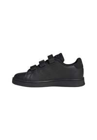 Zapatilla negra de corte bajo con tres tiras de velcro, paneles laterales perforados y suela texturizada, mostrada de perfil sobre un fondo blanco.