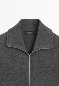 Grijze zip-up trui met een geribde kraag en textuur. Bevat een zilveren rits en een merklabel binnenin het nekgebied.