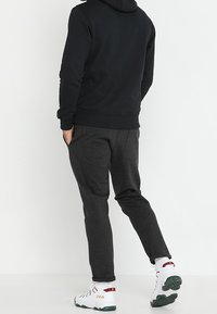 Felpa nera con cappuccio, pantaloni joggers grigi, polsini elastici e sneaker bianche con dettagli verdi. Design semplice e texture morbida. Logo del marchio ben visibile sulle scarpe.