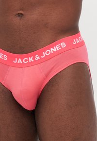 Ružové pánske slipy so širokým elastickým pásom s bielym nápisom "JACK & JONES", prezentujúce hladký, elastický materiál.