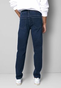 Dunkelblaue Jeans aus Denim mit geradem Bein. Merkmale sind zwei Gesäßtaschen, ein schwarzes Patch am Bund und eine strukturierte Stoffoberfläche.