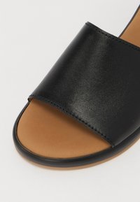 Black leather slide sandal with a wide strap and open toe, featuring a tan insole and a black rubber sole. Smooth surface texture.