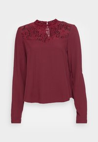 Blusa bordeaux a maniche lunghe con un colletto in pizzo, collo alto e dettaglio a chiave sul retro. Tessuto morbido, vestibilità rilassata e nessun motivo visibile.