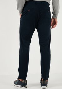 Navyblauwe katoenbroek met een slim fit, voorzien van twee achterzakken met rode accenten. De stof heeft een gladde textuur.