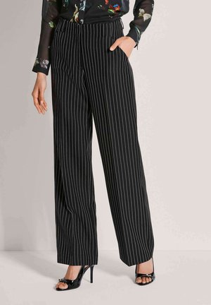 Zwart-wit gestreepte wijde broek met steekzakken aan de voorkant, gladde stof en een hoge taille. Gecombineerd met zwarte open-toe hakken.