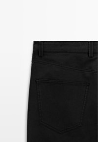 Czarne dżinsy z denimu o eleganckim kroju, z tylną kieszenią i detalicznym przeszyciem wzdłuż talii i krawędzi kieszeni.