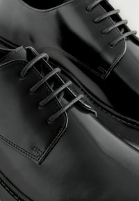 Schwarze, polierte Lederschuhe mit runden Zehen, sechs Ösen und schwarzen Schnürsenkeln. Glatte Oberfläche mit dezenten Steppnähten entlang der Nähte.