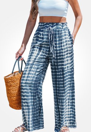 Pantalones de pierna ancha, teñidos en azul marino y blanco con efecto tie-dye, con cintura ajustable de cordón, confeccionados en tela ligera. Combinados con un bolso tejido naranja.