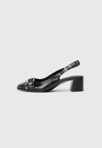 Melna ādas slingback apava kurpe ar norādītu pirkstu, dekoratīvām detaļām un masīnu papēdi. Iespējams, ir siksna ar apļveida akcentiem.