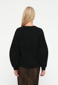 Sweater preto de malha com um padrão texturizado, mangas largas e decote redondo. Usado sobre uma saia de estampado de leopardo, com um corte descontraído.