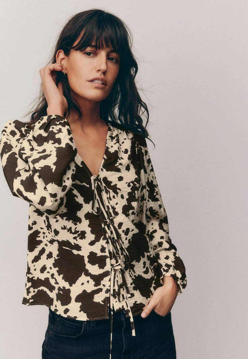 Brown and cream patterned blouse with a v-neckline, drawstring detail at the waist, and long sleeves with elastic cuffs.