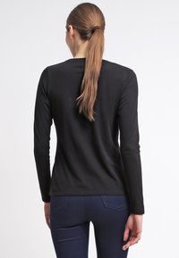 Musta pitkähihainen paita, joka on valmistettu sileästä kankaasta, yksinkertaisella kaula-aukolla ja vartalonmyötäisellä leikkauksella, nähtynä takaa.