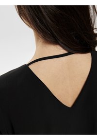 Blusa nera con scollatura a V sulla schiena e dettagli a spallina sottile. Texture liscia con sottili variazioni del tessuto.
