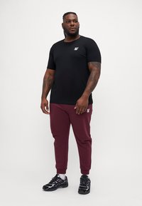 Cămașă neagră cu mânecă scurtă și un logo mic, asortată cu pantaloni de trening bordeaux. Întregul outfit este completat cu adidași negri cu accente albe.