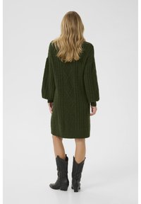 Abito maglione di colore verde scuro con motivo a trecce, maniche lunghe e vestibilità rilassata, abbinato a stivali cowboy neri.