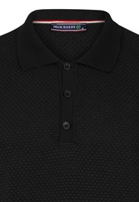 Mustmustärk, millel on tekstureeritud muster, kolm nuppu ja kontrastse kaelusega, millel on punased ja valged triibud. Brändi silt on nähtav.