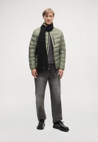 Προστατευτικό μπουφάν σε ελαιόλαδο πράσινο χρώμα, μαύρο κασκόλ, γκρι φούτερ και γκρι τζιν με εφέ φθοράς. Μαύρα παπούτσια με παχύ πέλμα. Απλός, λειτουργικός σχεδιασμός.