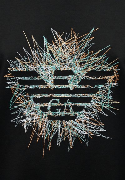 Το μαύρο ύφασμα διαθέτει ένα ζωντανό, αφηρημένο κεντημένο σχέδιο σε τυρκουάζ, πορτοκαλί και λευκό, κεντραρισμένο γύρω από στιλιζαρισμένο κείμενο και δυναμικές γραμμές.