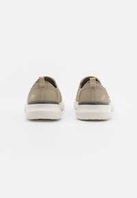 Beżowe buty sportowe z siateczkowym wierzchem, miękką białą podeszwą i uchwytami z tyłu dla łatwego zakładania. Minimalistyczny design z detalem logo.