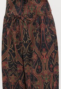 Tecido preto com padrões que apresentam intrincados designs paisley em vermelho, verde e dourado. Inclui um laço na cintura e elementos texturizados.