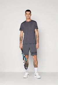 Meeste spordiriietus: tumehall lühikeste varrukatega särk ja sobivad püksid, millel on "BORG" logod, tennisereket käes.