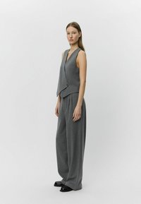 Gray sleeveless vest with a wrap design and button detail paired with wide-leg gray trousers made of a soft, textured fabric.