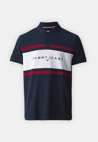 Camisa polo para hombre en color marino con rayas horizontales blancas y rojas. Presenta un cuello y una tapeta de botones, con el logo de "TOMMY JEANS" exhibido de manera prominente.