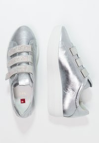 Zilveren sneakers met een metallic leren afwerking, voorzien van drie klittenbandsluitingen versierd met heldere rhinestones en een witte rubberen zool.