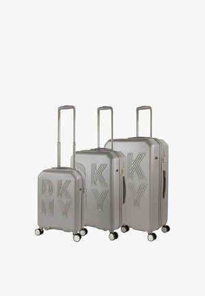 Tres maletas DKNY con acabado plateado metálico, que presentan un logo en relieve, asas telescópicas y ruedas multidireccionales.
