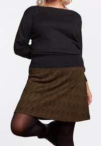 Svart långärmad tröja med vid halsringning, i kombination med en brun mönstrad A-linje kjol med vågiga linjer. Svarta strumpbyxor och ankelstövlar.