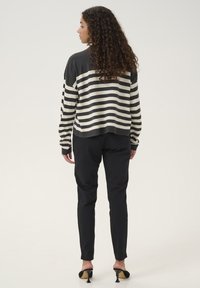 Gestreifter Pullover in Schwarz und Creme, lässige Passform mit gerippten Bündchen, kombiniert mit maßgeschneiderter schwarzer Hose und offenen Pumps.