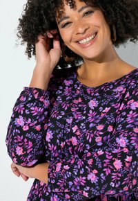 Czarna sukienka z żywym różowo-fioletowym kwiatowym wzorem, z długimi bufkami i okrągłym dekoltem. Gładka faktura tkaniny.