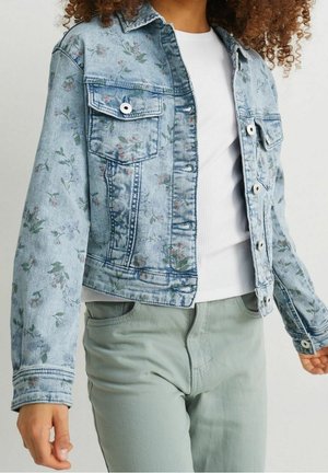 Denimjakke med lys blå vask, blomsterprint i pink og grøn, to brystlommer og knaplukning. Båret over en hvid skjorte.