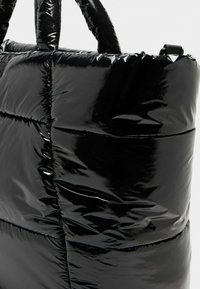 Borsa tote nera in stile piumino con finitura lucida, caratterizzata da sezioni trapuntate e superficie liscia, manici doppi e una tracolla sicura.