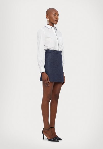 White long-sleeve shirt with contrasting collar detail, paired with a dark denim mini skirt and black stiletto heels.