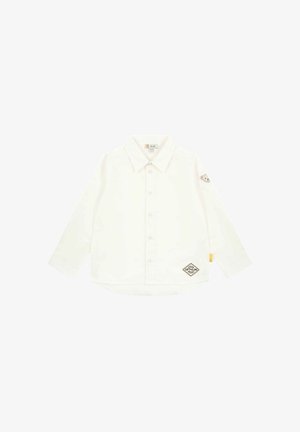 Biała koszula z długim rękawem, zapinana na guzik, z kołnierzykiem, z brązową łatą od misia na rękawie oraz logo na dole. Miękka tekstura.