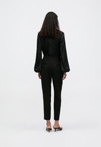 Blusa preta com mangas volumosas combinada com calças pretas ajustadas. O modelo usa mules pretos de salto. Tecido suave, silhueta elegante.