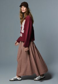 Burgundia värvi pika varrukaga dressipluus valge kirjaga, kombineeritud pika ruudulise seelikuga ja valgete tossudega, millel mustad detailid. Pruun kork.