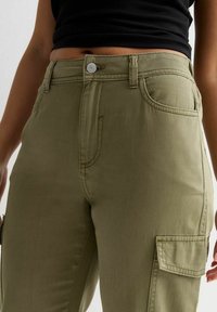 Kaki cargobroek met een aansluitende taille, voor- en zijzakken en zichtbare stiksels. De stof is zacht met een gladde textuur.