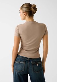 Dopasowany beżowy top z krótkim rękawem o miękkiej fakturze, zestawiony z ciemnoniebieskimi dżinsami z kieszeniami na zamek i kontrastującymi przeszyciami.
