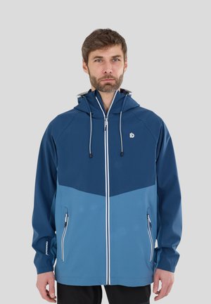 Man draagt een tweekleurige blauwe capuchonjas met een rits aan de voorkant en ritszakken, staand tegen een effen lichtgrijze achtergrond.