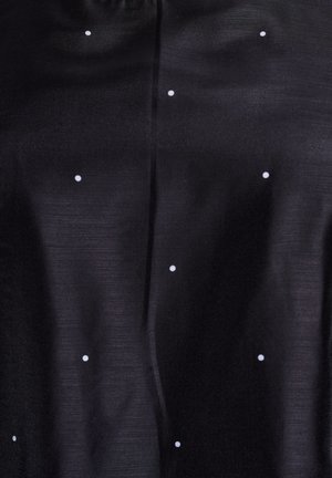 Tela negra con textura suave y lunares blancos esparcidos. El diseño incluye un brillo sutil y detalles de costura vertical.