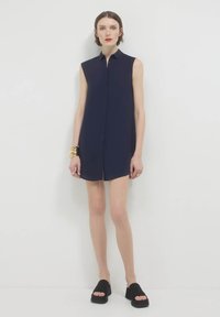 Abito chemisier senza maniche di colore blu navy con bottoni sul davanti, colletto a punta e spacchi laterali; tessuto morbido e vestibilità comoda; abbinato a sandali platform neri.