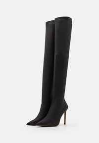 Botas de tacón alto negras hasta la rodilla, confeccionadas en un tejido suave, con un diseño de punta afilada y un acabado sin costuras, que presentan un tacón delgado y alto.