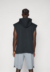 Hoodie senza maniche nera con un cappuccio ampio, realizzata in un tessuto morbido, abbinata a pantaloni corti grigi chiari con fessure laterali per una maggiore libertà di movimento.