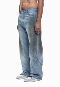 Svetlo modre široke kavbojke iz jeansa z zbledelim učinkom, z edinstvenimi šivi in sproščenim krojem. Kombinirane z belimi supergami.