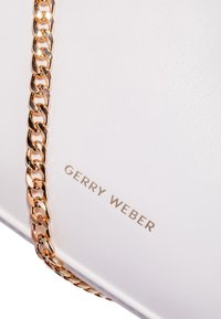 Hvid håndtaske med tekstureret læder, udstyret med en metalisk guld kædestropp og præget "GERRY WEBER" logo i guld i bunden.