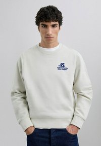 Sweatshirt gri deschis cu guler rotund, manșete côtotate și un logo brodat albastru pe pieptul stâng. Textură netedă și croială relaxată.