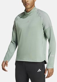 Lichtgroen atletisch top met lange mouwen, hoge kraag, gestructureerde stof en subtiele logodetail. Coördinerende donkere broek met logoaccent.